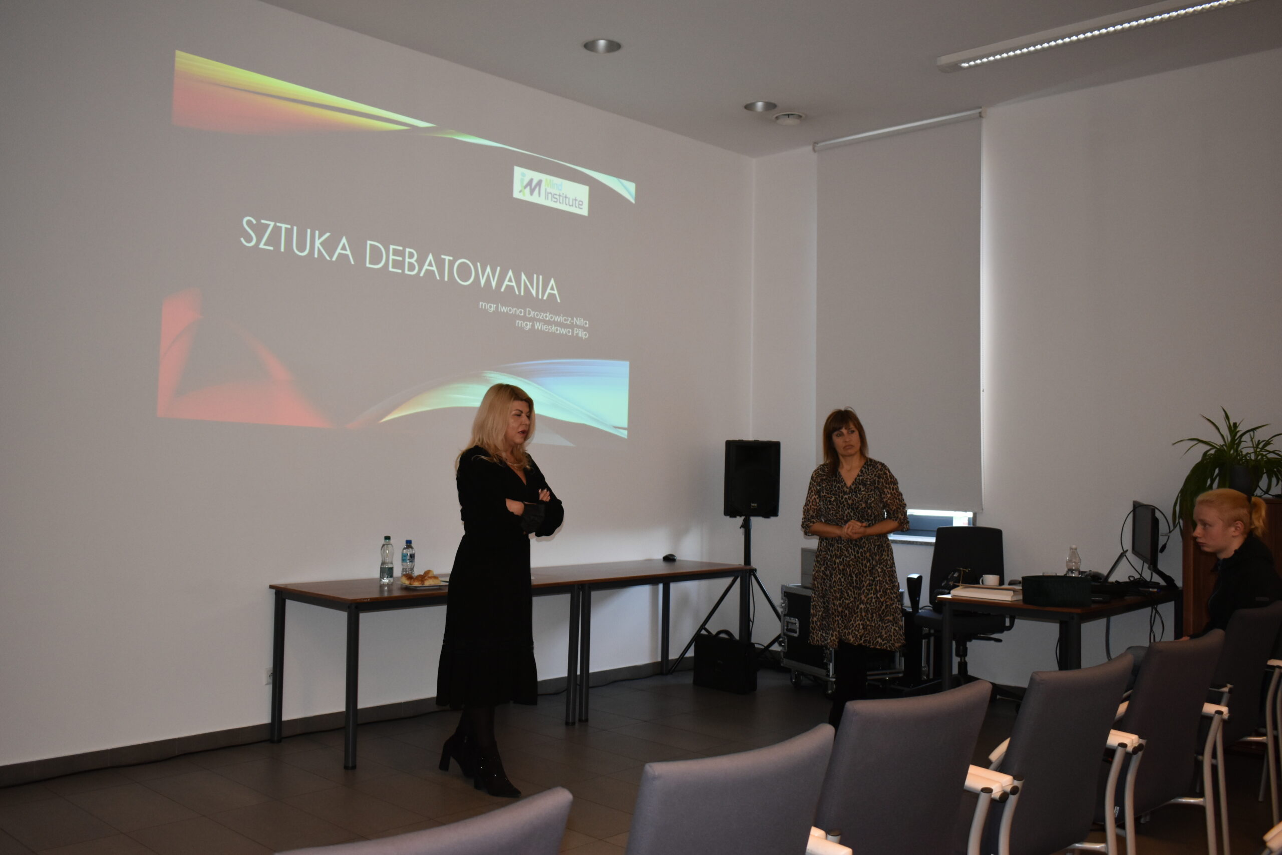 Wiesława Pilip i Iwona Drozdowicz-Nita prowadzą szkolenie dla młodzieży. W tle pokaz slajdów.